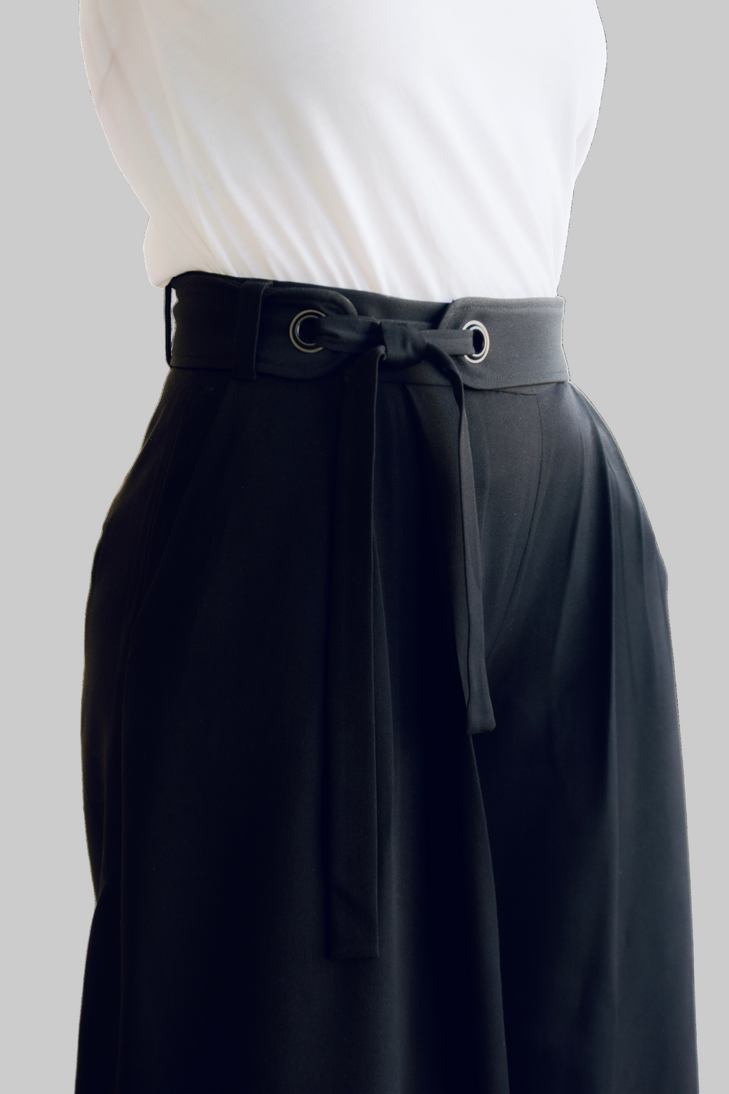 Close-up of MØRKE Siv Palazzo Trousers — high-waisted black viscose-blend pants featuring an adjustable belt with metal eyelets, front pleats, and tailored waistband. Detail shot highlighting construction and fit.