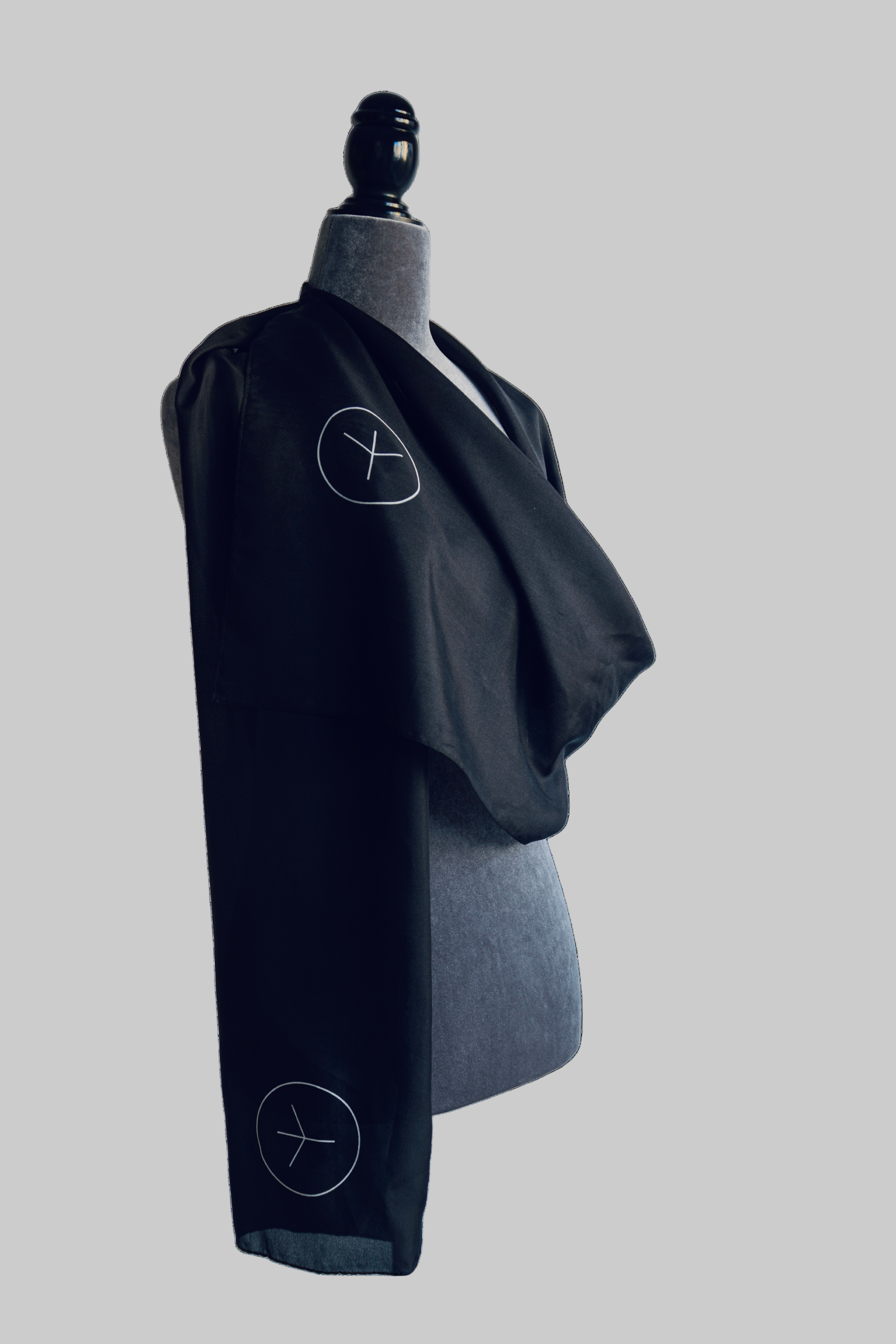 MØRKE Rán Stola — luxury handmade habotai silk scarf in black, lightweight and translucent, featuring subtle rune symbols. Premium 180×40 cm accessory inspired by Nordic mythology, shown draped on a mannequin for fit and flow. Rán silk stola by MØRKE — handmade 100% habotai silk scarf crafted in South Korea, inspired by the Nordic goddess of the seas. Black, soft, and translucent with minimalist rune details; 180 cm long and 40 cm wide, draped elegantly on a mannequin.